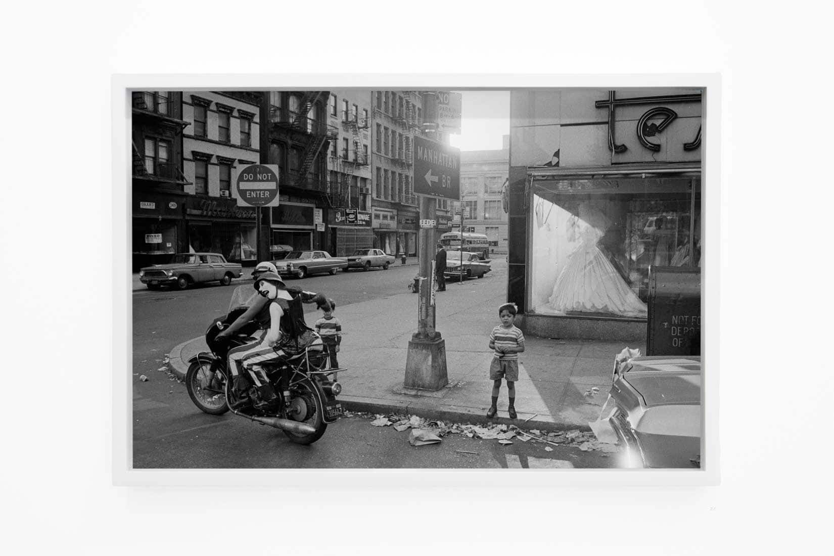 Black and white photo of a motorbike with a mannequin on the back passing a child on the street.