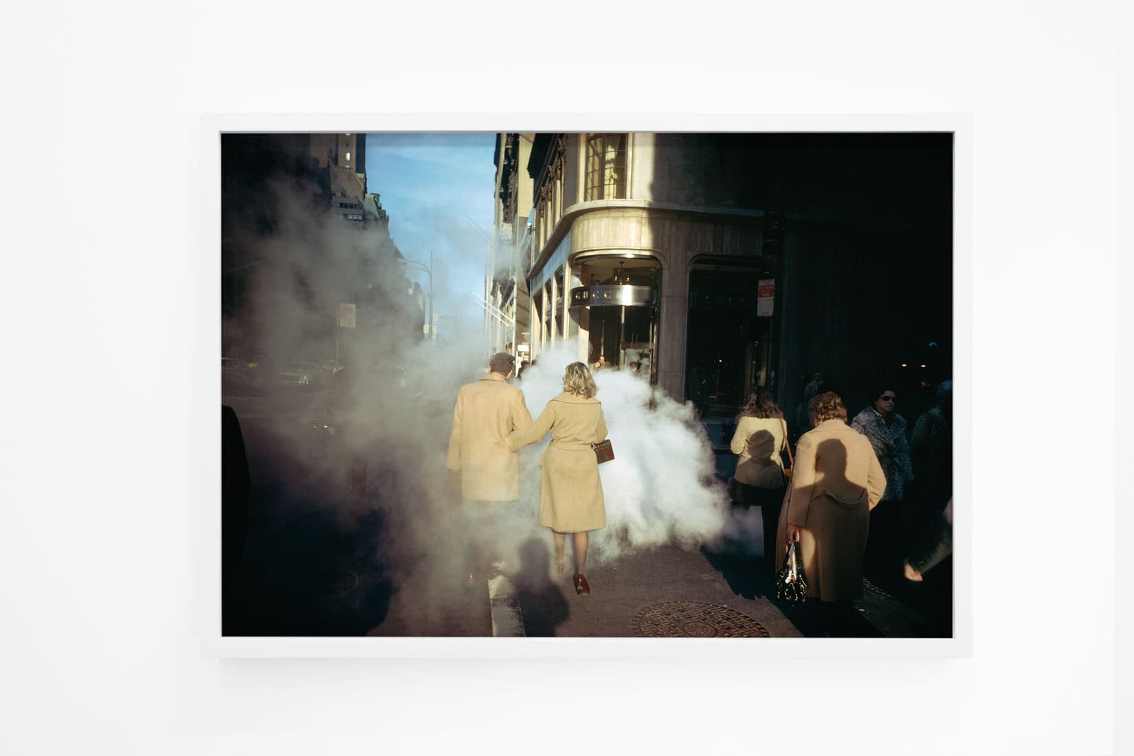 Photo of a couple wearing coats walking through smoke on a street.
