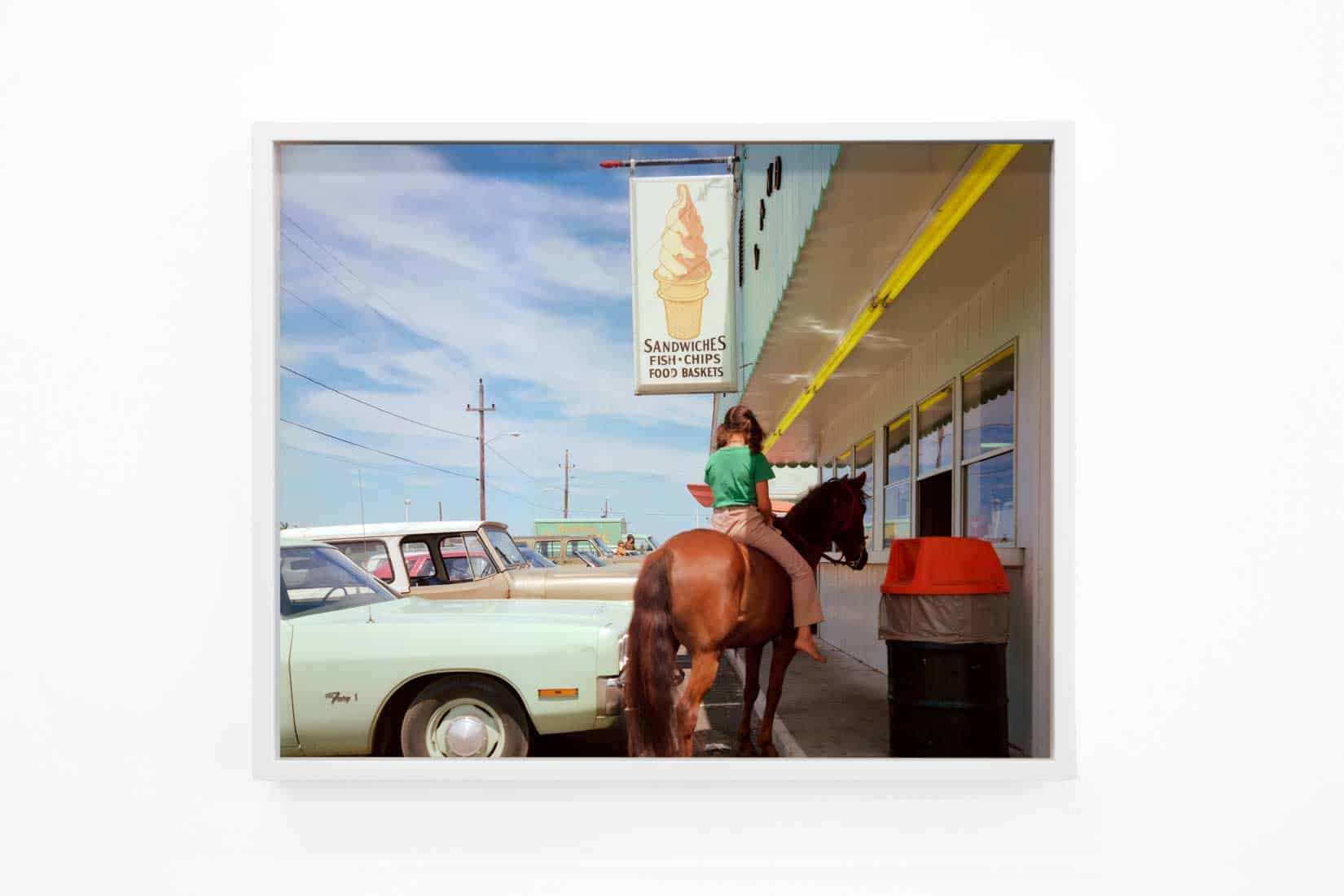Photo of a girl on a horse in a parking lot.