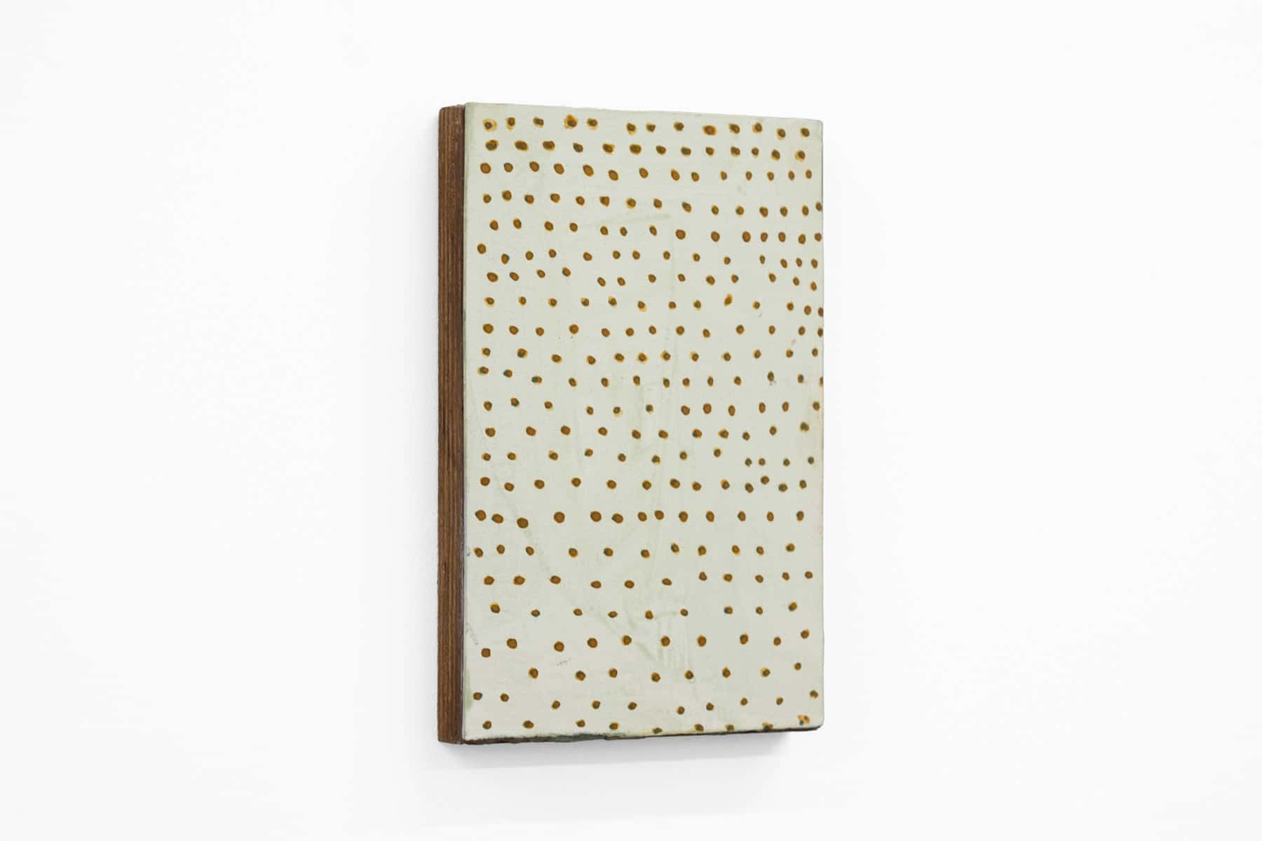 Abstract painting of green brown specks on cream paper and wood.